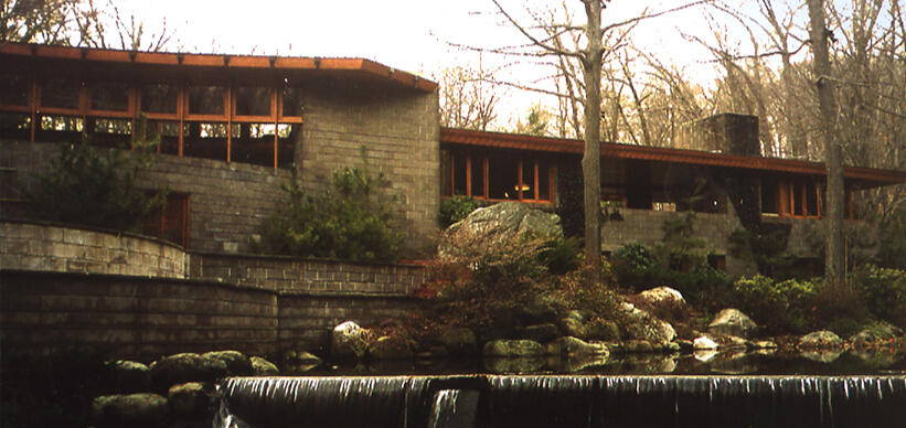 frank lloyd wright's palatial home, a tranquil house (comprised of bricks and wood support) resides near a small body of water with trees